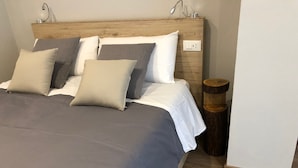 A neatly made bed with a wooden headboard, multiple pillows, and a bedside table with a lamp. - PETITE MAISON: 50 steps from the cable car !!! (Courmayeur)