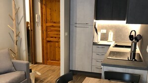 A compact living space with a kitchenette, a dining table with chairs, a grey sofa, and a wooden door. - PETITE MAISON: 50 steps from the cable car !!! (Courmayeur)