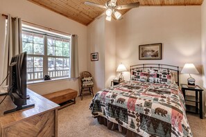 Un dormitorio con cama, escritorio, silla, ventilador de techo y ventana con cortinas.