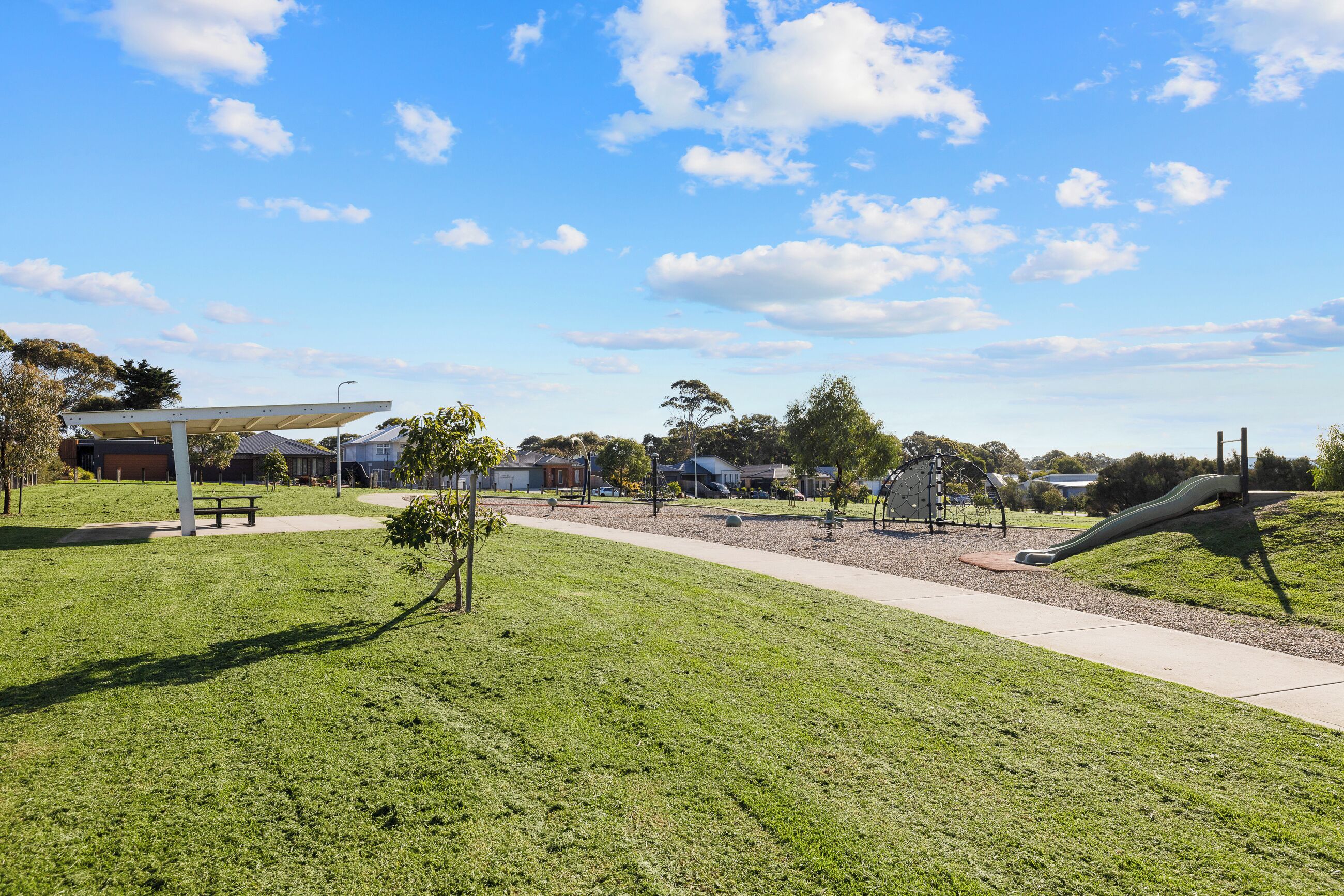 Ein Park mit einem Spielplatz, einer überdachten Sitzgelegenheit und einem Weg.
