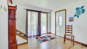 A room with a wooden staircase, a wooden chair, a colorful rug, and a door with a decorative sign. - Waterfront Lake Erie Vacation Rental on the Strip! (Geneva-On-The-Lake)