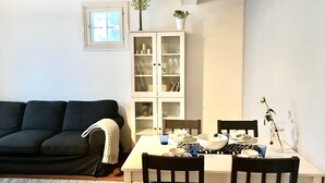 Ein Wohnzimmer mit einem dunkelgrauen Sofa, einem weißen Schrank mit Glastüren und einem Esstisch mit Stühlen.