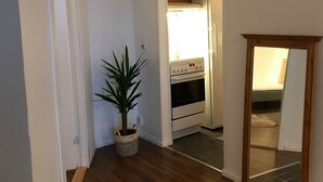 Ein Flur mit Holzbalkendecke, einem Blumentopf, einem gefliesten Boden und einem durchgehenden offenen Durchgang zum Küchenbereich.