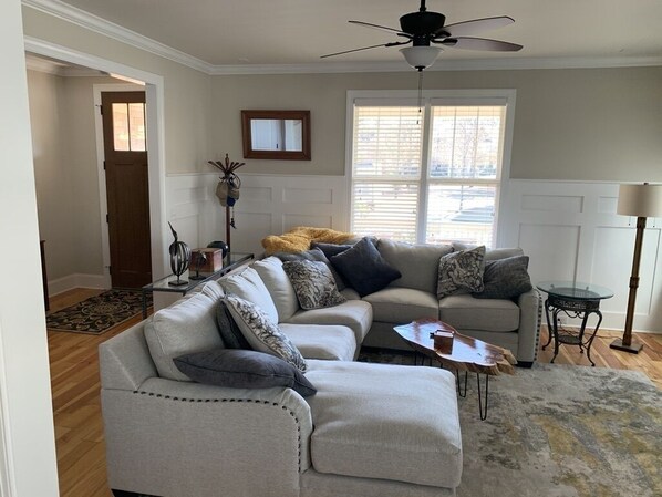 A living room with a sectional sofa, a ceiling fan, a window with blinds, and a floor lamp.