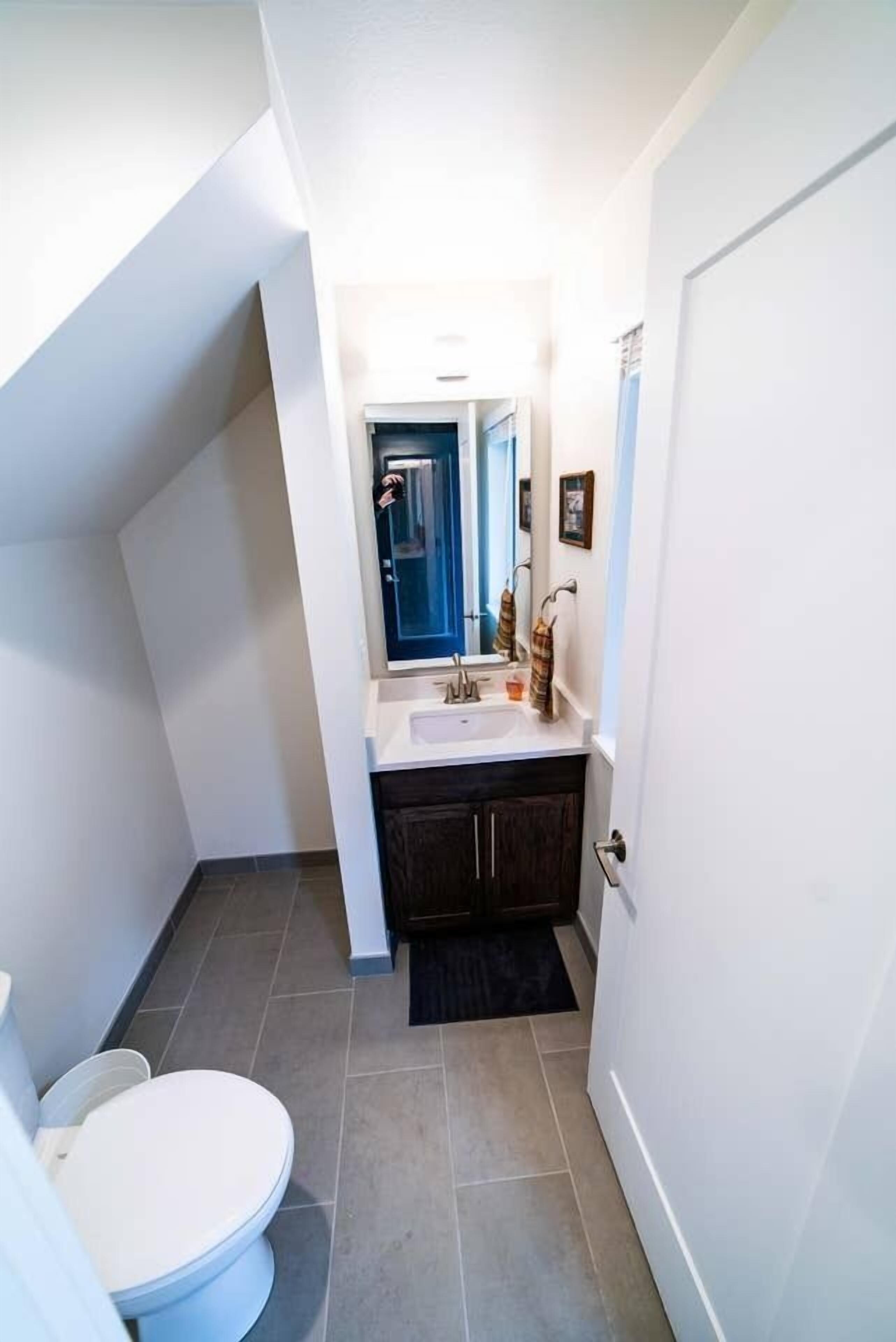 A compact bathroom with a white toilet, dark wooden cabinets, a white sink, and a mirror above the sink.