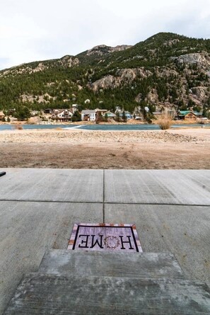 A concrete deck with a "HOME" mat in the foreground and a mountainous landscape with houses in the background. - The Snowberry Sanctuary Lakefront Georgetown (Georgetown)