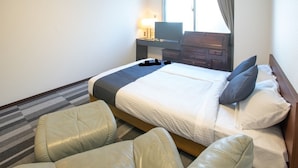 Una habitación de hotel con una cama, dos sillas, un escritorio con lámpara y un televisor.