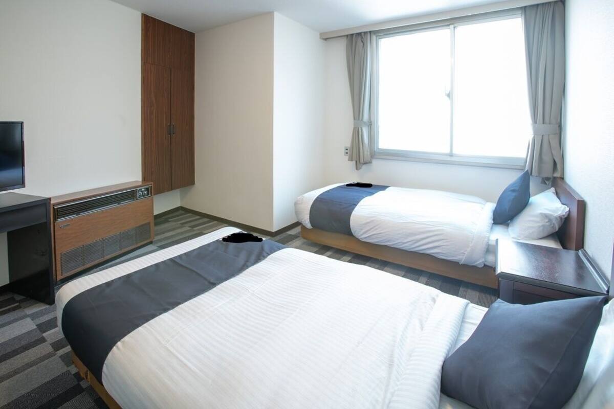 A hotel room with two beds, a TV, a wardrobe, and a window with curtains.