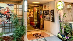 Entrada de una tradicional posada japonesa con puerta corredera, felpudo y cartel con caracteres japoneses.