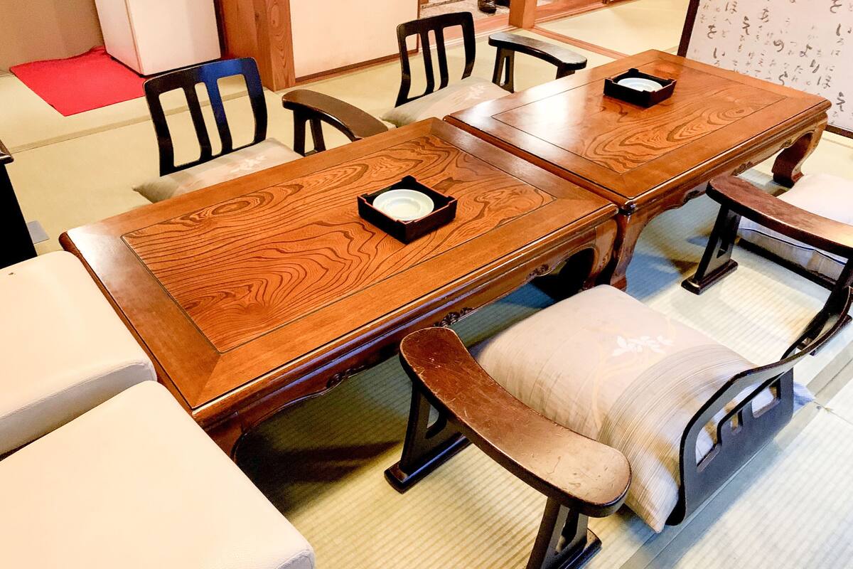 A traditional wooden dining table with matching chairs, a small tray, and a red mat on the floor.