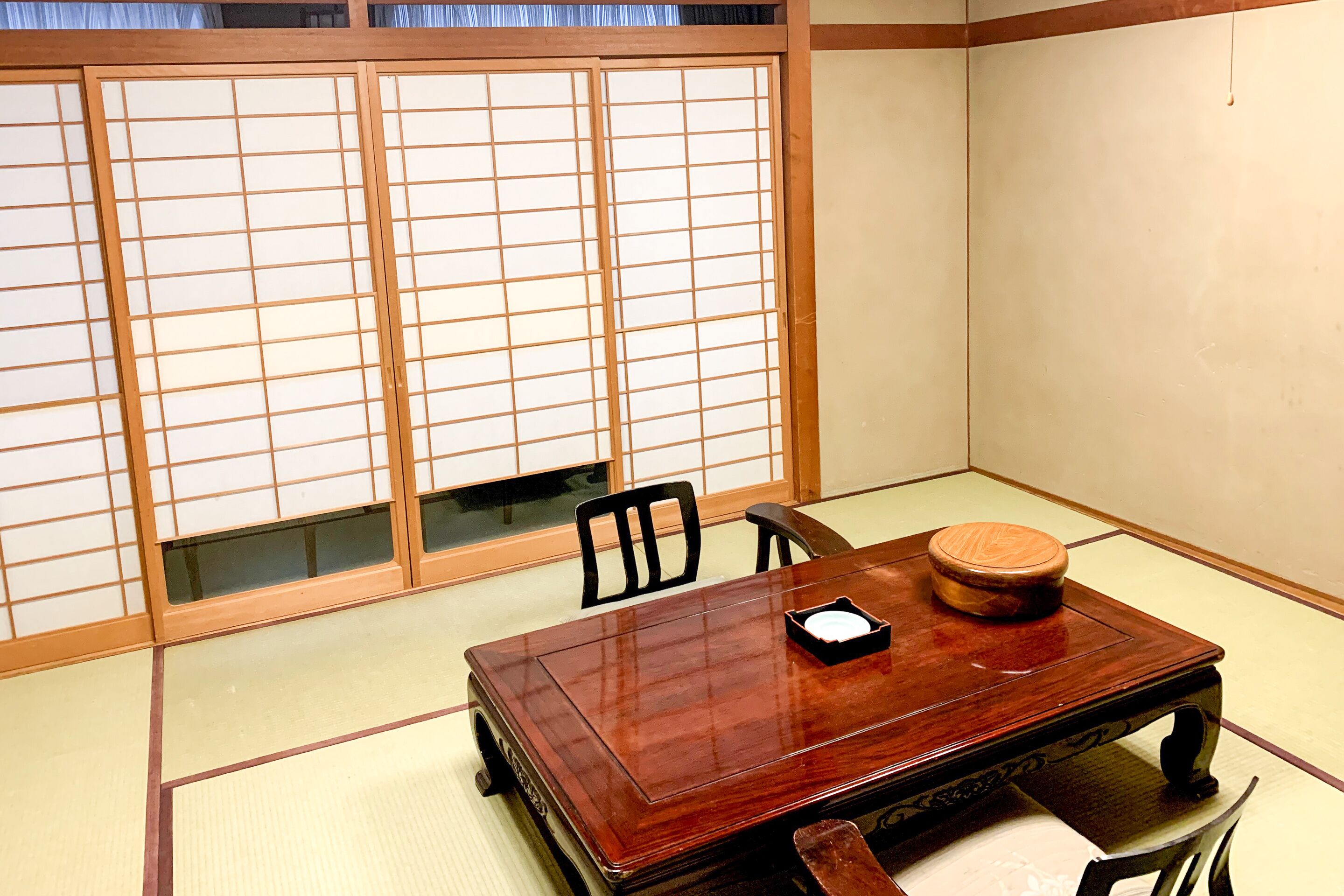 Une pièce de style japonais traditionnel, avec un sol recouvert de tatamis, une table en bois et une porte coulissante à motifs géométriques.