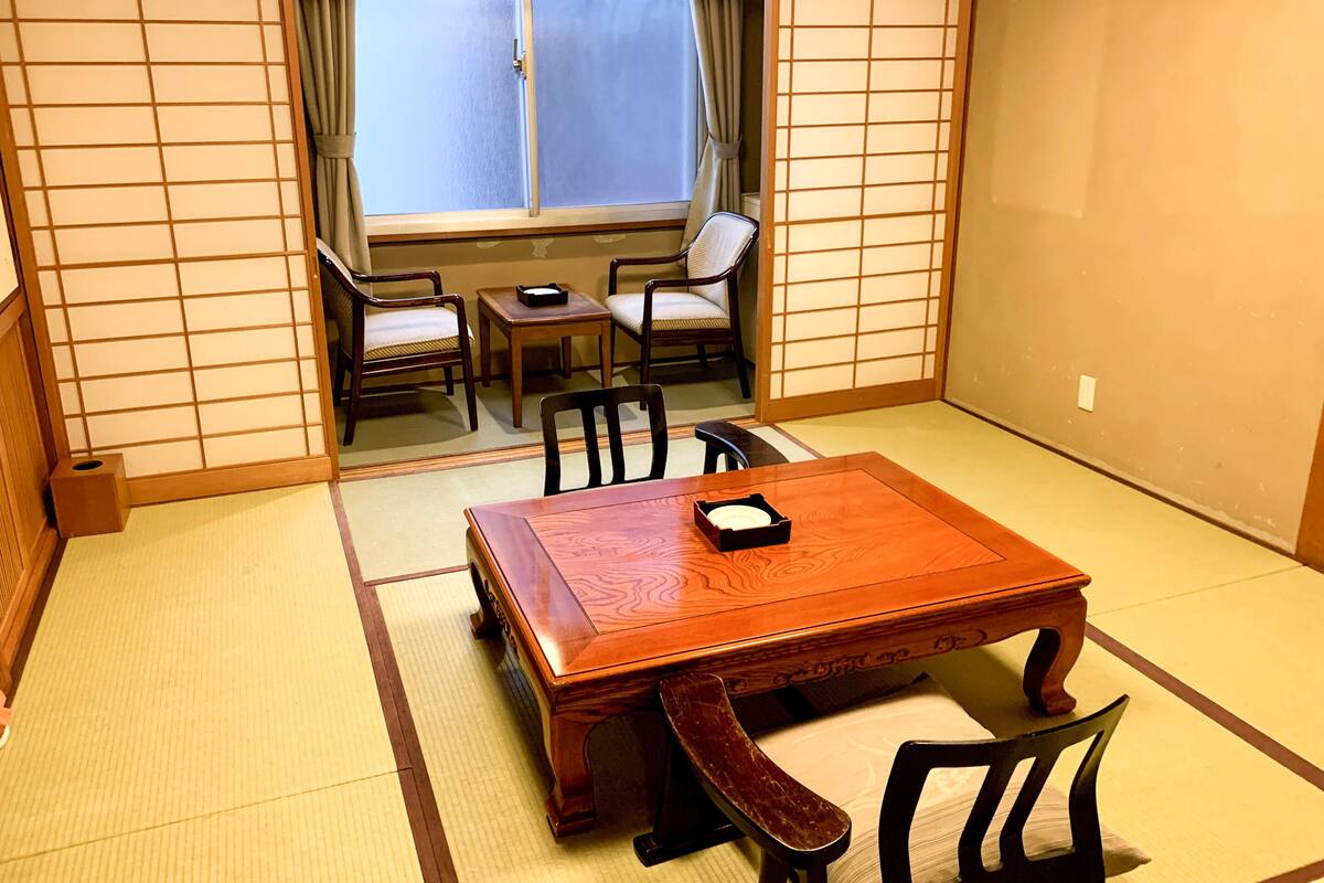 A traditional Japanese room with tatami flooring, a wooden table, and two chairs.