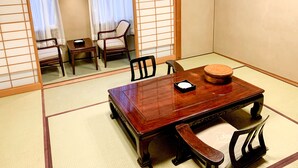 Una habitación japonesa tradicional con suelo de tatami, una mesa de madera con cojín y dos sillas.