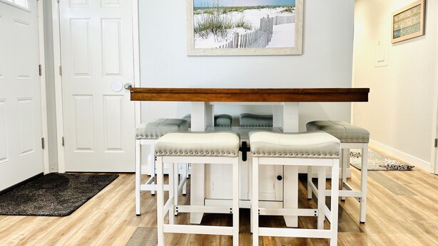 A dining area with a white table and four barstools, a wooden bench, and a framed picture on the wall.