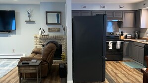A modern kitchen with grey cabinets, a black refrigerator, and a dining area with a brown leather couch.