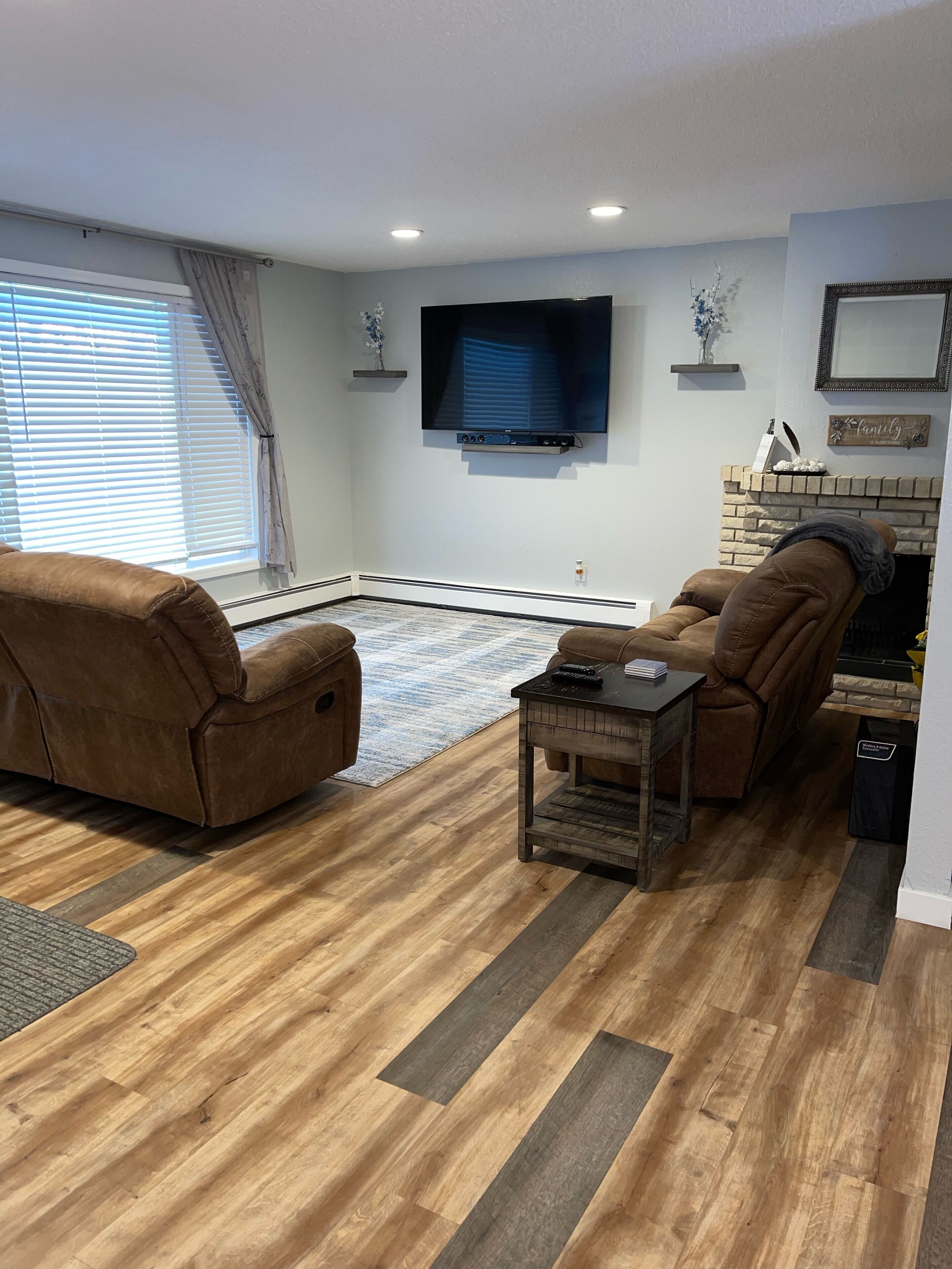 Een woonkamer met een open haard, een flatscreen televisie aan de muur en twee bruine leren fauteuils.