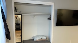 A compact bedroom with a grey sofa bed, a flat-screen TV mounted on the wall, and a small table with a lamp and decorative items.