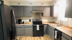 A modern kitchen with grey cabinets, a stainless steel refrigerator, a black oven, and a wooden floor.