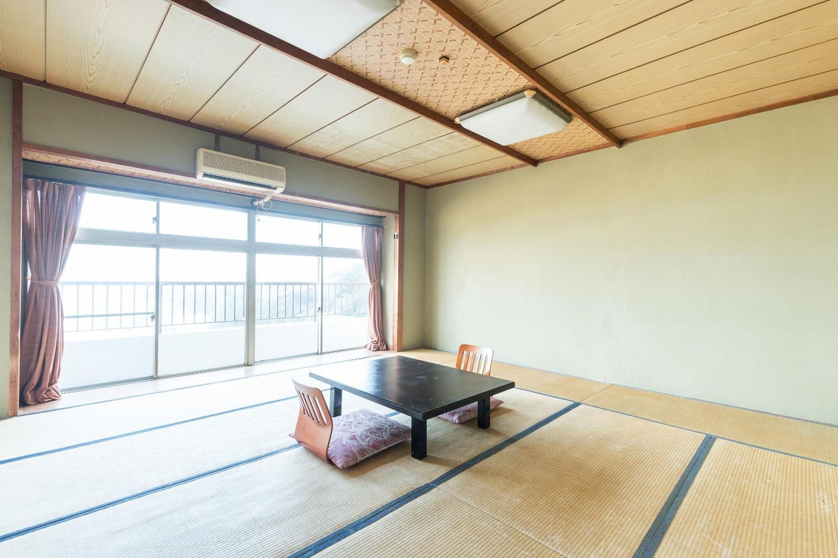 A room with tatami mats, a low table, and chairs. There is a sliding door with a view to the outside.