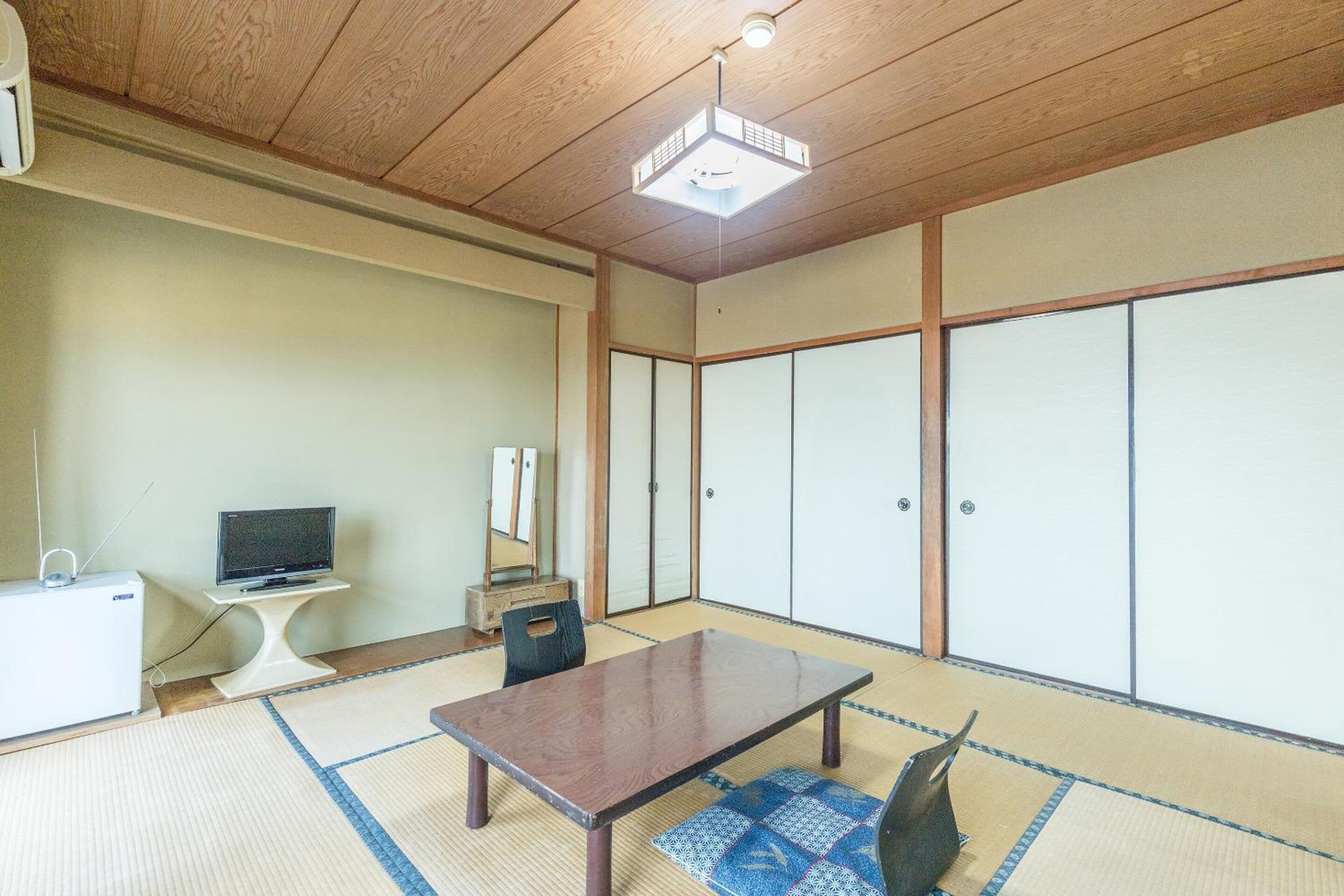 A traditional Japanese room with tatami flooring, a low table, a television on a stand, and sliding doors.