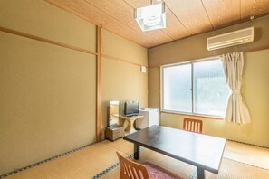 Traditional Japanese-style room with tatami flooring, featuring a low table, chair, TV, and large window with a curtain.