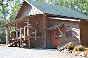 Eine Holzhütte mit Veranda, einer roten Tür und einem kleinen Fenster.