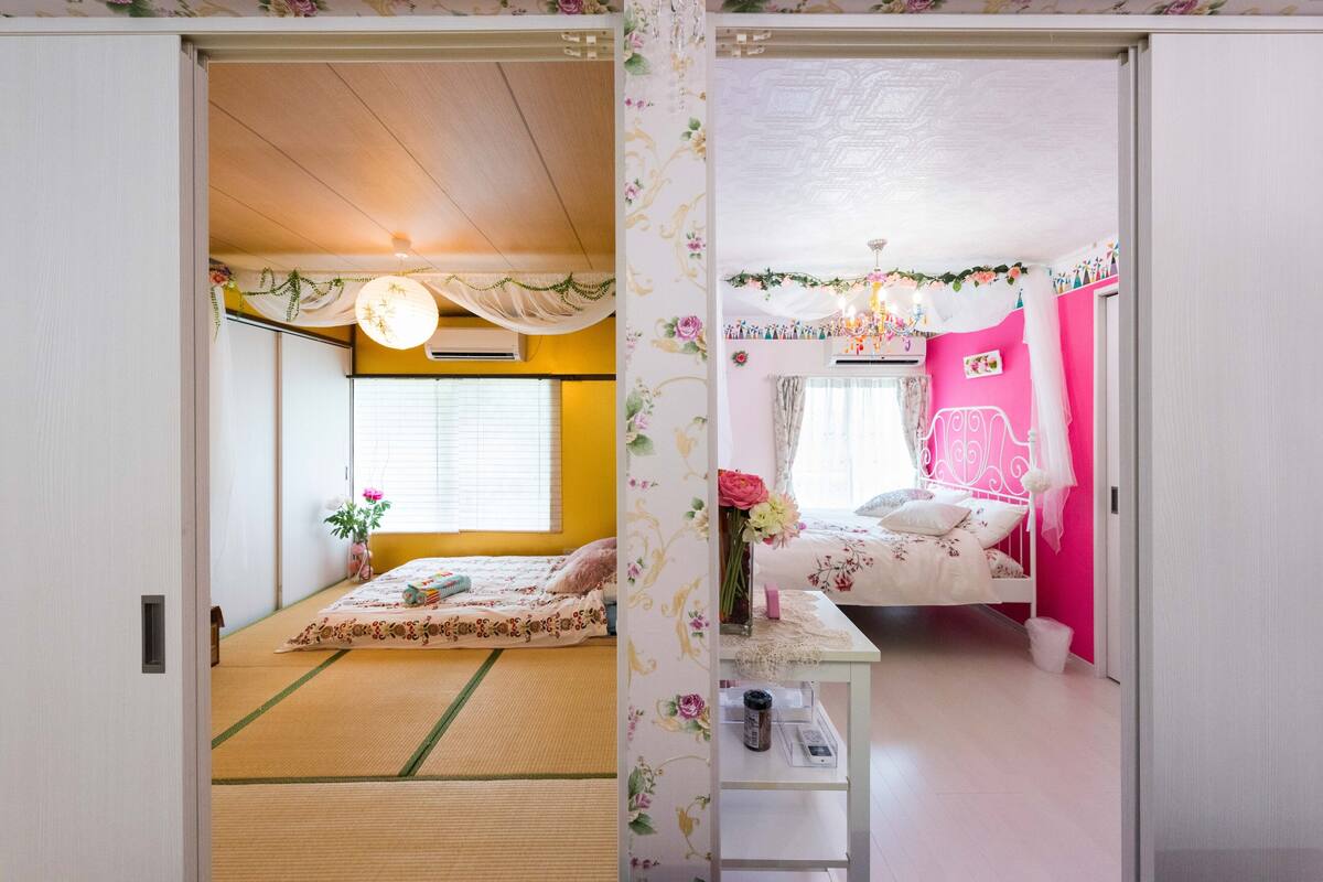A traditional Japanese room with tatami flooring, a bed with floral bedding, and a small table with a vase.