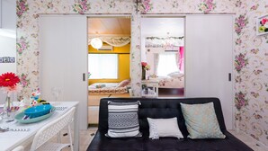 Et værelse med blomstret tapet, en sort sofa med mønstrede puder, et hvidt bord med en blå bakke og en seng med blomstret sengetæppe.