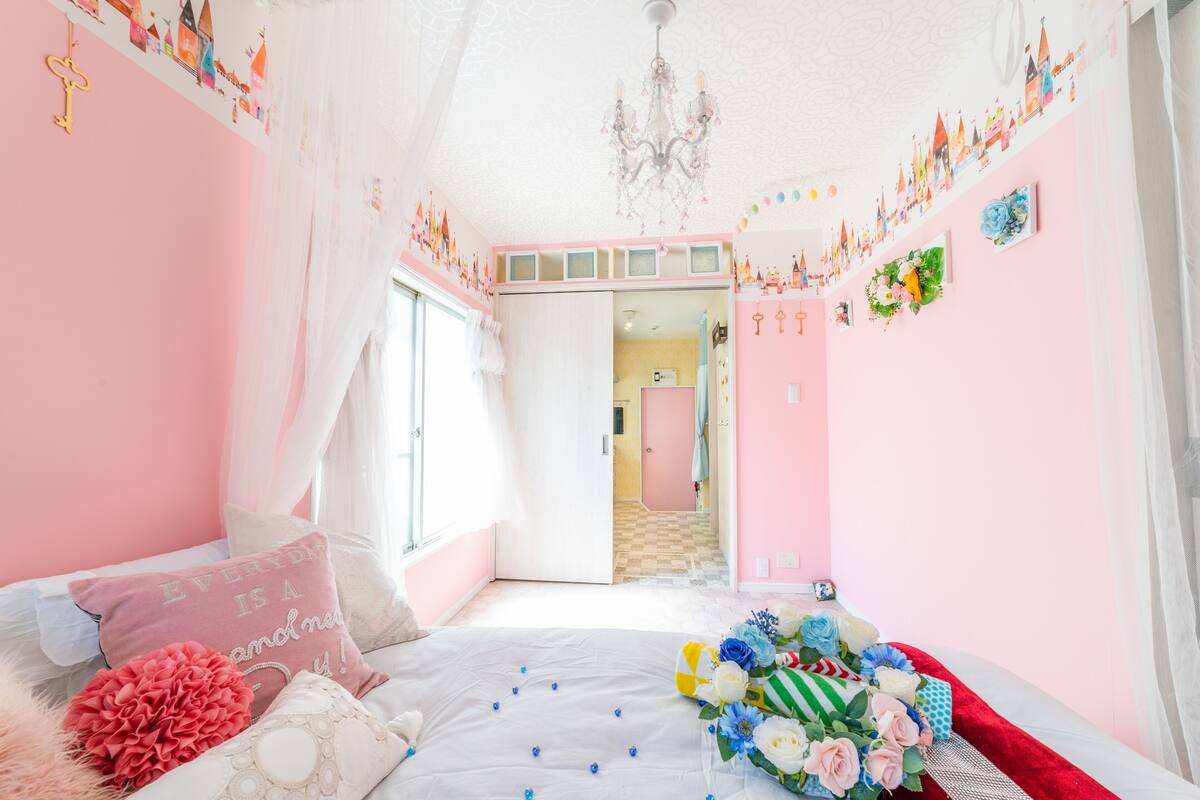 A pink-themed bedroom with a bed, pillows, and a bouquet of flowers.