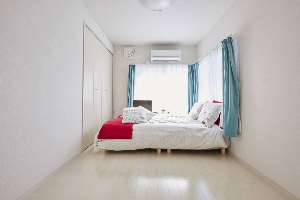 A bedroom with a bed, curtains, an air conditioning unit, and a window.
