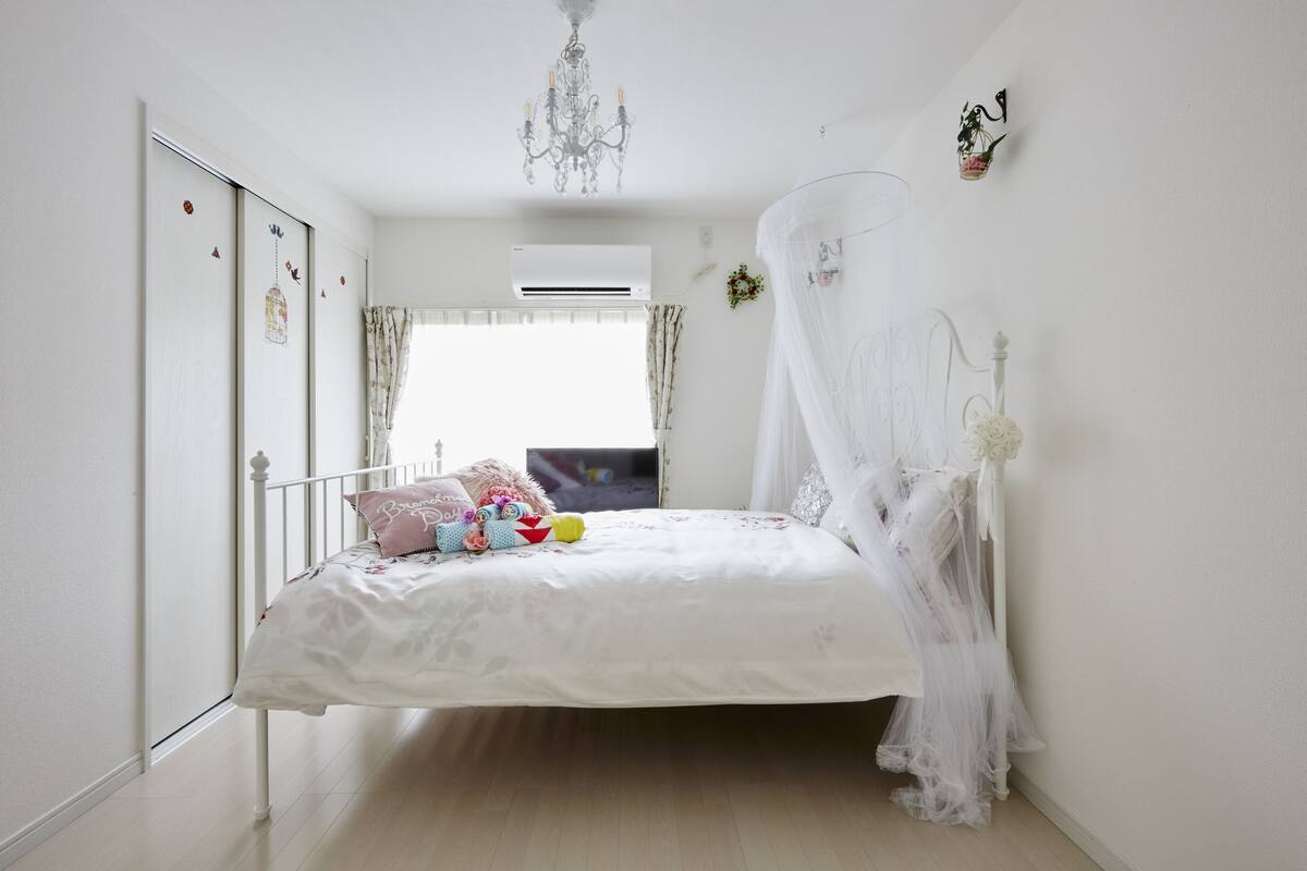A bedroom with a bed, a chandelier, a window with curtains, and a wall-mounted air conditioner.