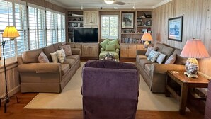 A living room with two sofas, a TV, wooden cabinets, and a ceiling fan. - Old Pamlico Inn Site:  Large waterfront home with dock, amazing views (Ocracoke)