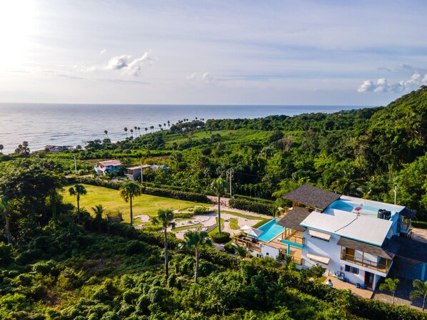 Une maison moderne avec piscine, entourée d’une végétation luxuriante et offrant une vue sur l’océan.