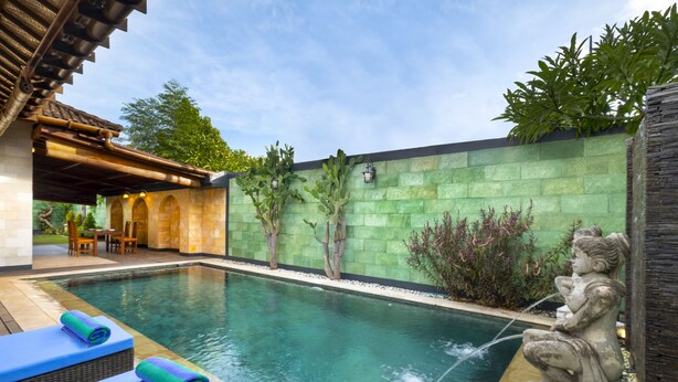 A swimming pool with a stone wall, a statue, and a covered seating area. - Villa Sotra Description (Denpasar)
