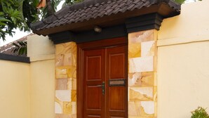 A wooden door with a stone facade, flanked by steps and greenery. - Villa Sotra Description (Denpasar)