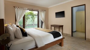 A bedroom with a bed, a bedside table, a TV mounted on the wall, and a door leading to another room. - Villa Sotra Description (Denpasar)