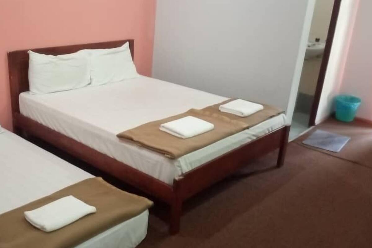 A hotel room with two single beds, each with white linens and a brown throw blanket.