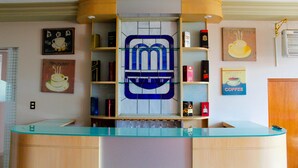 Zona de recepción con mostrador de cristal, logotipo azul y estantes con productos de café y té.