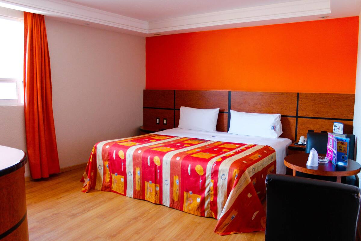 Une chambre d’hôtel avec un lit, une petite table, une chaise et une fenêtre avec des rideaux.