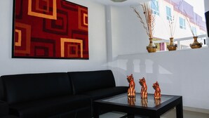 Una sala de estar moderna con un sofá negro, una mesa de centro de vidrio y tres figuritas decorativas de gatos.