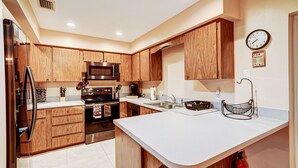A kitchen with wooden cabinets, stainless steel appliances, a white countertop, and a clock on the wall. - Home Away From Home   (Boynton Beach)