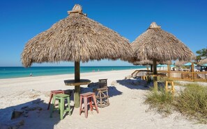 Ein Strand mit Reetdachschirmen und Holzstühlen.