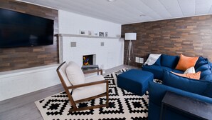 Un salon moderne avec un téléviseur à écran plat, une cheminée, un canapé bleu et un tapis à motifs.