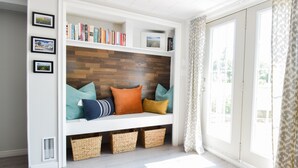Une pièce dotée d’une banquette intégrée, d’étagères, de paniers en osier et offrant une vue sur l’extérieur grâce à une grande fenêtre.
