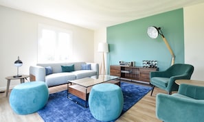 A modern living room with a sofa, ottomans, a coffee table, a lamp, a radio, and a clock on the wall.