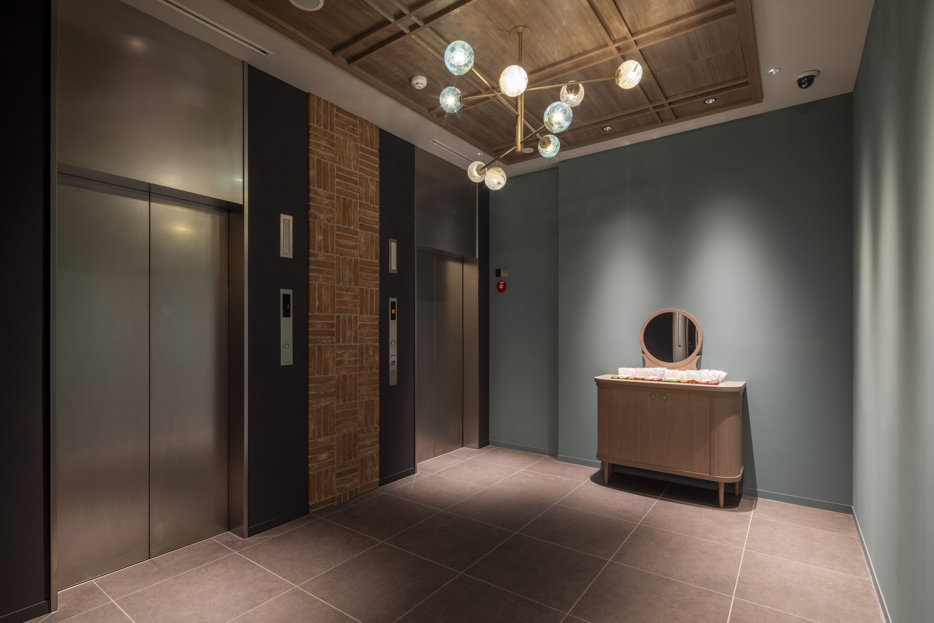 A modern elevator area with a wooden panel wall, a wooden vanity with a mirror, and a ceiling light fixture.