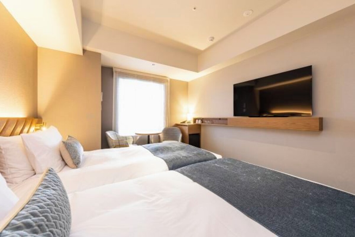 Una habitación de hotel moderna con una cama grande, un televisor montado en la pared y un escritorio con una silla.