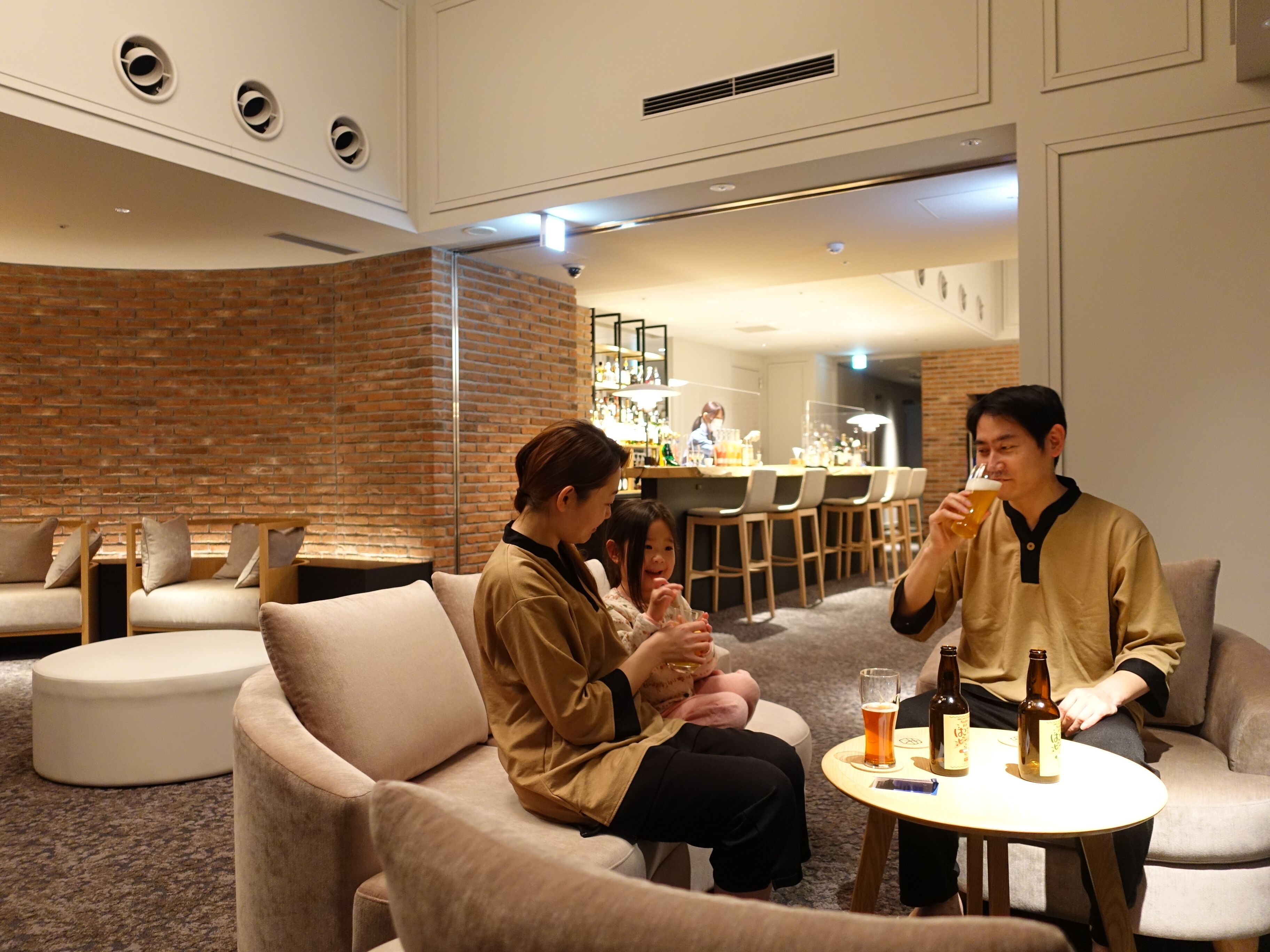 Un espace de détente moderne avec des canapés, une table ronde sur laquelle sont posées des bouteilles, et un bar en arrière-plan.