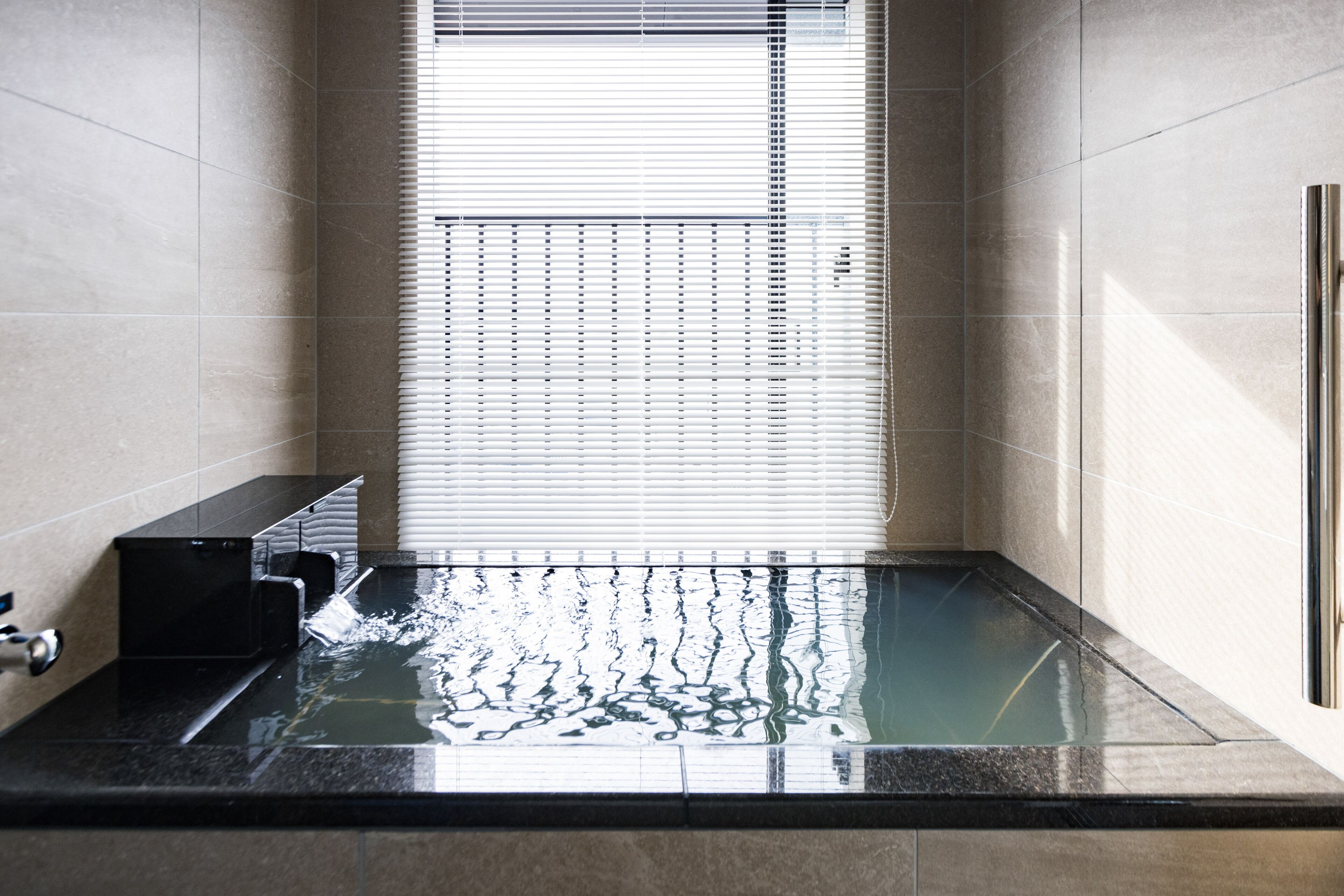 A modern bathroom with a glass-enclosed shower, a black sink, and a window with blinds.