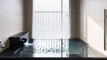 A modern bathroom with a glass-enclosed shower, a black sink, and a window with blinds.